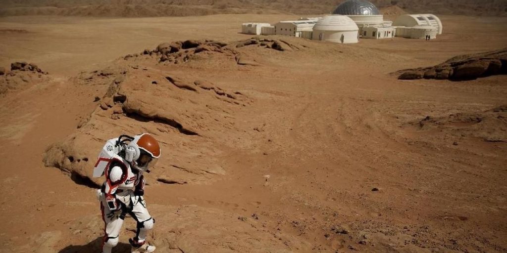 Suited Explorer Walking Across Red Desert Rock Near A Domed Research Base